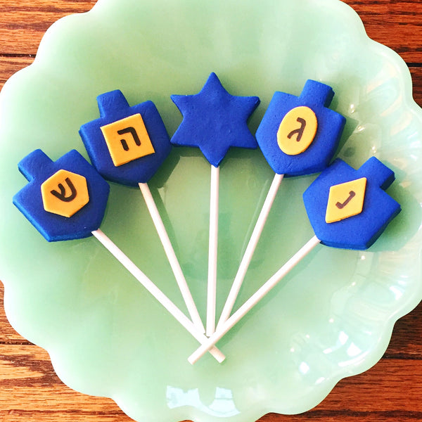 Hanukkah blue dreidels with gold letters in menorah shape marzipan candy lollipops in a candid shop